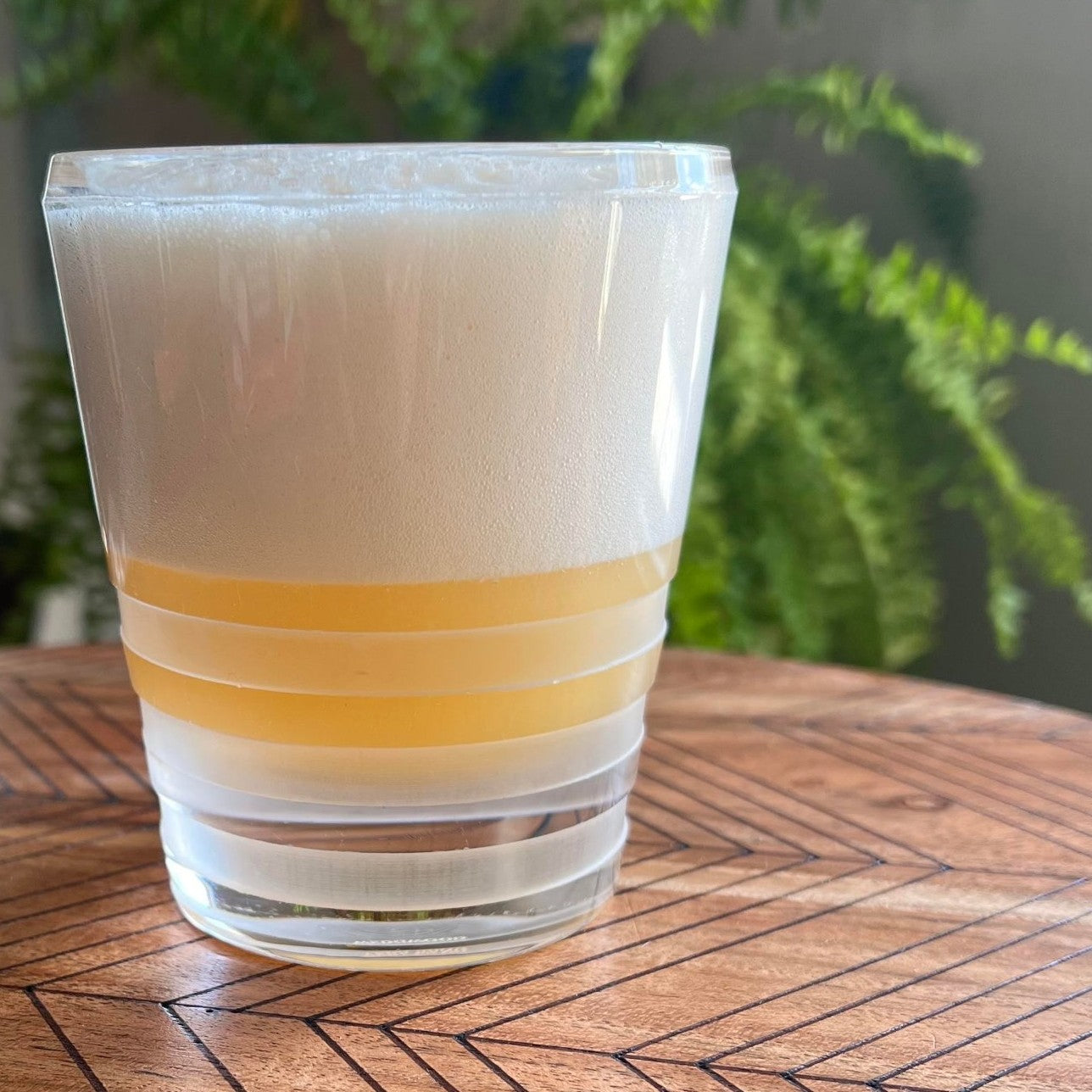 A frothy Gin Fizz in a frosted rocks glass on a wood table
